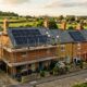 Cotswold stone terraced houses in Oxfordshire with solar panels being installed and scaffolding, representing energy efficiency upgrades for the Warm Homes Fund